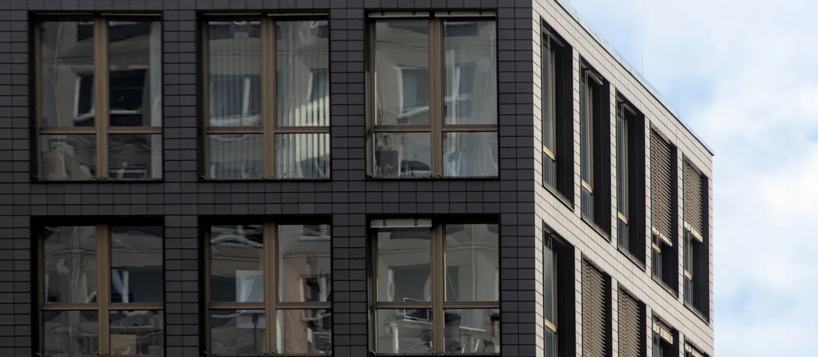 Moderner Bürobau mit dunkler Klinkerfassade und großen Fensterrahmen, daneben ein hellerer Flügel vor bewölktem Himmel